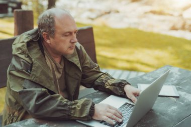 Yetişkin bir avcı açık havada netbook ile oturuyor