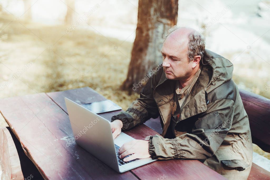 An aged man with the netbook is sitting outdoor