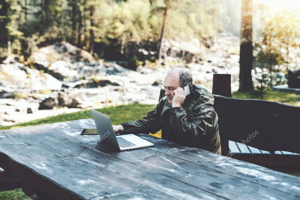 Man entrepreneur with laptop talking on the phone in forest