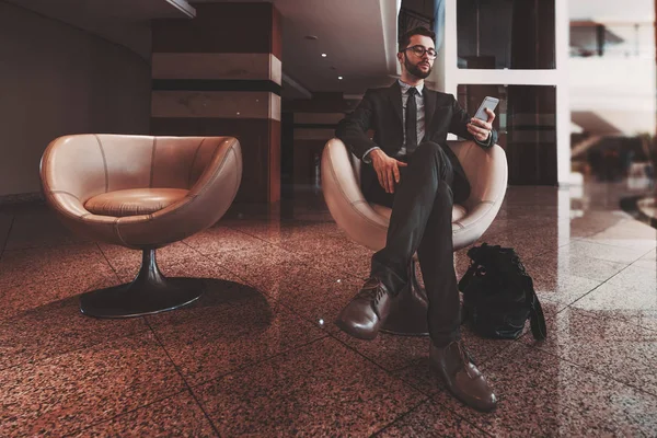 Бизнесмен со смартфоном в кресле в помещении — стоковое фото