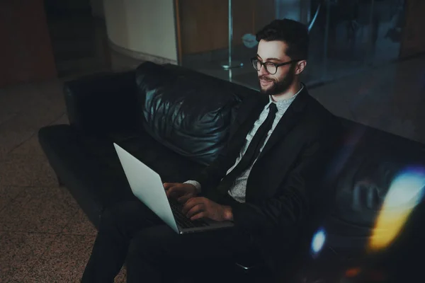 Улыбающийся бизнесмен на офисном диване с нетбуком — стоковое фото