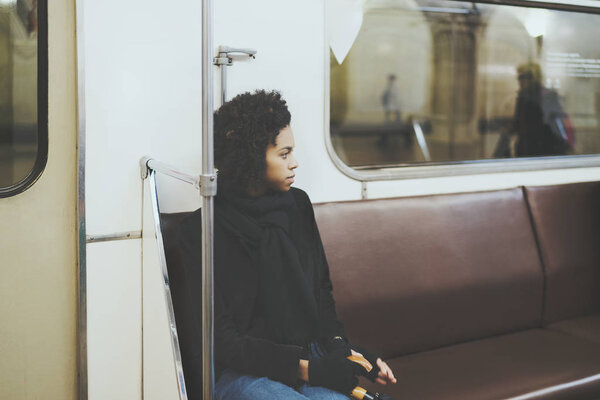 Black curly girl in metro carriage, looking aside