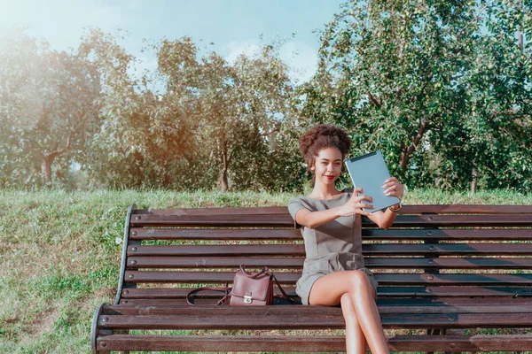 Mujer brasileña sonriente con tableta digital en un jardín público —  Fotos de Stock