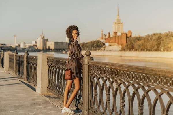 Czarna dziewczyna ze sprzęgłem, w pobliżu rzeki Moskwy podczas zachodu słońca — Zdjęcie stockowe