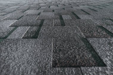 Soft roof tiled gray grainy texture on the top of a summer house lit by the sun; grey soft roofing tiles covering a building, focus on the middle distance clipart