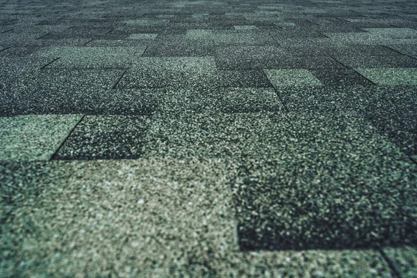 Soft roof tiled greenish grainy texture on the top of a summer house lit by the sun; green soft roofing tiles covering a building, focus on the middle distance