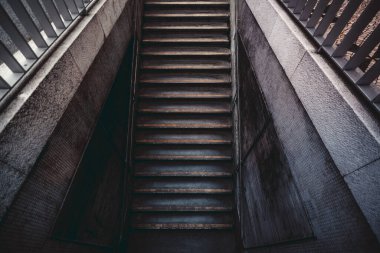 Karanlık bir yeraltı geçidine ya da geniş açılı metro girişine doğru beton adımları olan uzun ve modern bir merdiven; fayanslı duvarları olan dar şehir merdivenleri.