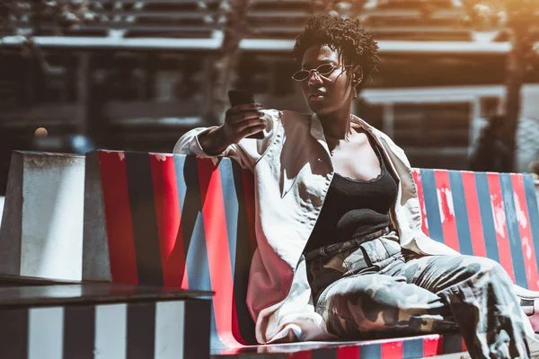 Elegant Young African Female Using Her Cellphone While Sitting Striped — Φωτογραφία Αρχείου