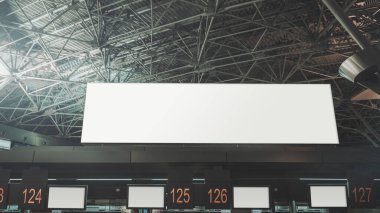 Modern bir havaalanı terminalinin kalkış bölgesinde, varış-kalkış bilgisi için boş beyaz ekran şablonlarıyla birden fazla numaralandırılmış kontrol gişelerinin üzerinde uzun yatay boş bir reklam panosu modeli.