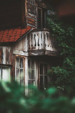 Dikey çekim, sığ bir alan derinliği ile eski, sığ bir ön cephe, iki katlı bir yazlık balkon ve desenli bir çit, sağdaki Rowan ağacı gölge düşürür.