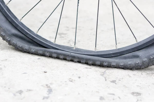 Bicycle wheel with flat tyre on the concrete road.