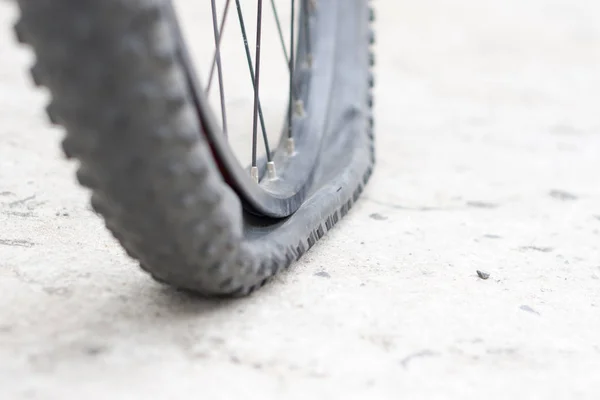 Bicycle wheel with flat tyre on the concrete road.