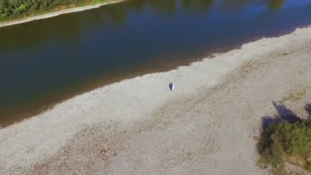 Pasangan pengantin yang cantik berjalan di sepanjang tepi sungai. Menembak dengan drone — Stok Video