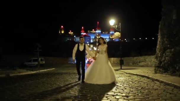 Um belo castelo numa colina. Palácio fortificado nas rochas à noite. Torres com uma luz de fundo vermelho-azul. O casal beija no fundo do castelo . — Vídeo de Stock