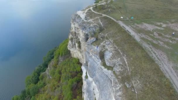 Nagy naplemente a tó, a hegyek között. Egy pár átölelve a szikla szélén. 4k. Légi — Stock videók