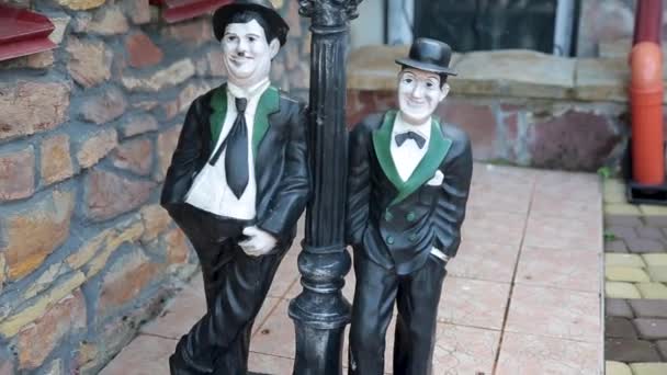 Duas estatuetas de comediantes apoiadas numa lâmpada de rua . — Vídeo de Stock