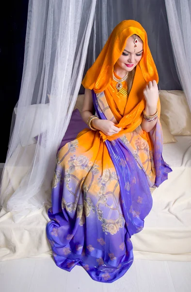 Mujer rubia joven en un brillante saris indio y joyas sentado bajo una cabeza modestamente abatida valance —  Fotos de Stock