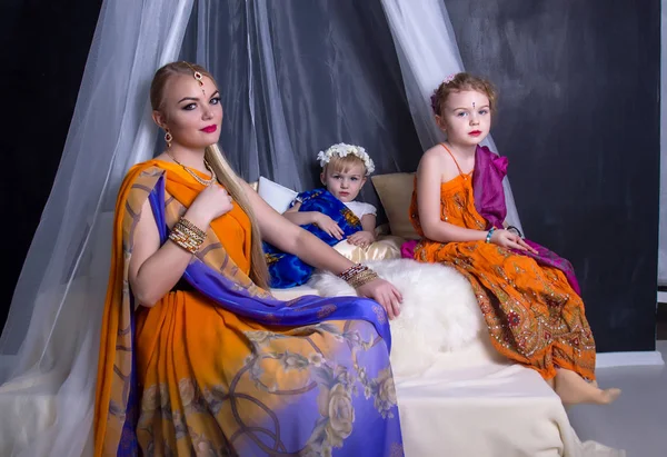 Joven rubia en un brillante saris indio y joyas sentada bajo un valance transparente con dos hijas jóvenes — Foto de Stock