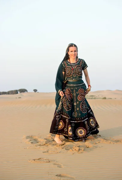 A young woman in Indian national clothes laughs joyfully, walking barefoot in the sand dunes of the Tar desert. Rajasthan, India. — Stock Photo, Image