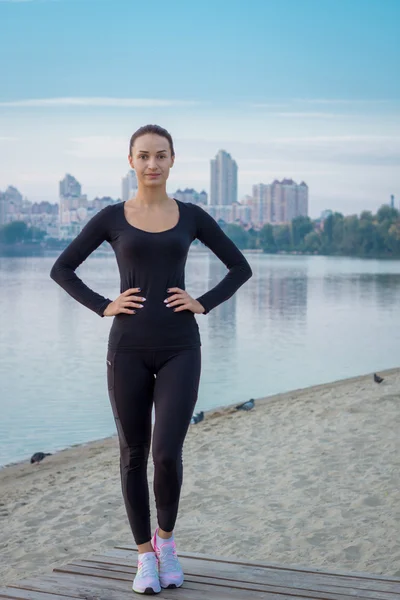 Young fitness woman stands on pier at morning sunrise — ストック写真