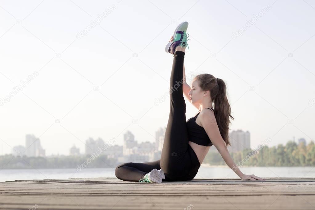 Fitness girl stretches her legs during sport workout exercises o