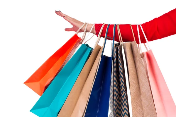 Embalagens de compras multicoloridas e brilhantes penduradas no braço feminino de mangas vermelhas — Fotografia de Stock