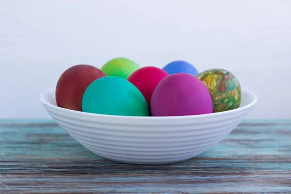 Λευκό πιάτο με πολύχρωμα Πασχαλινά αυγά σε φόντο ξύλινη — Φωτογραφία Αρχείου