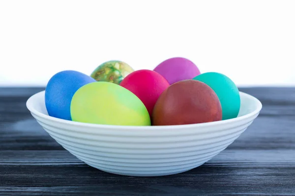Λευκό πιάτο με πολύχρωμα Πασχαλινά αυγά σε μαύρο ξύλινο έκφραση — Φωτογραφία Αρχείου