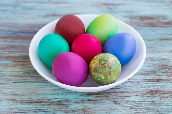 Witte plaat met Pasen versicolored eieren op houten achtergrond — Stockfoto