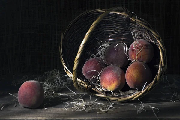 Stillleben mit Pfirsichen im Weidenkorb auf einem Holztisch. — Stockfoto