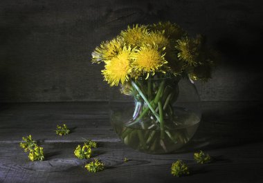 Bir cam vazo dandelions ile ahşap bir masa üzerinde duruyor.