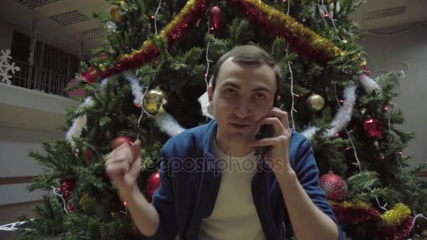 Hombre de teléfono inteligente que llama en el teléfono móvil contra el fondo del árbol de Navidad — Vídeos de Stock