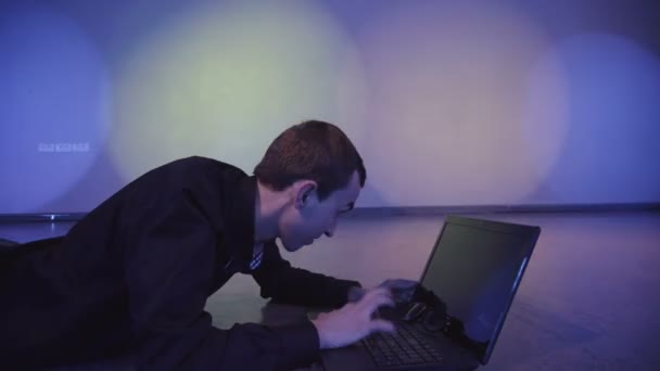 A young man typing on a keyboard of switched off laptop, and lying on the floor at nightclub — Stock Video