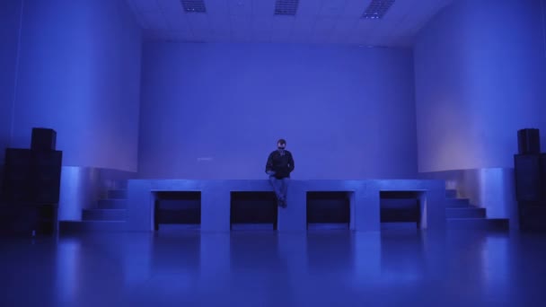 Egy fiatalember egyedül ül egy üres tánc padló, és használ a laptop, hogy meghívja barátait egy fél — Stock videók