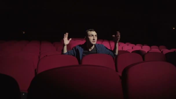 Hombre sentado en cómodas sillas rojas en un cine oscuro, viendo la actuación y preocupado — Vídeos de Stock
