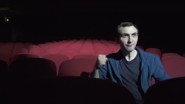 Homem sentado em confortáveis cadeiras vermelhas em um cinema escuro, assistindo ao desempenho e preocupado — Vídeo de Stock