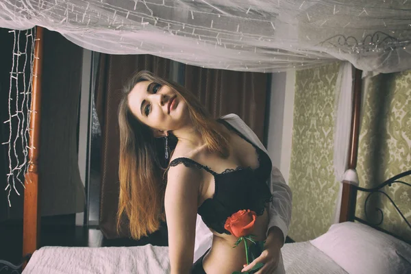 Bir beyaz erkek gömlek ve siyah sütyen reklam külot giymiş seksi kadın yatakta oturur