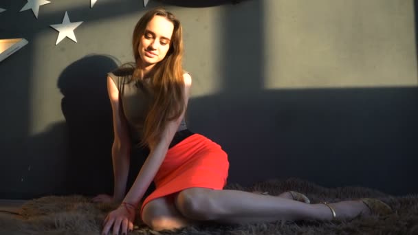 Aantrekkelijk meisje, zittend op de vloer tapijt in een avondjurk op een zonnige dag binnenshuis — Stockvideo