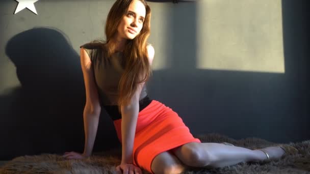 Приваблива дівчина сидить на підлозі килима в вечірній сукні в сонячний день в приміщенні — стокове відео