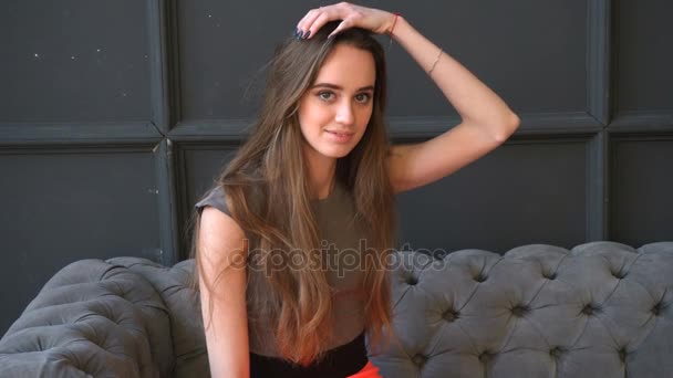 Menina bonita no vestido está sentado no sofá cinza macio — Vídeo de Stock