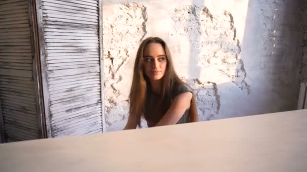 Долли снимок красивой девушки, сидящей за роялем, освещенным солнечным светом из окна — стоковое видео