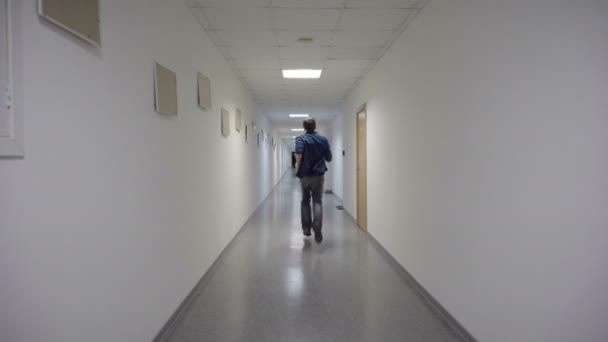 El hombre escapa al final de un largo corredor blanco — Vídeos de Stock