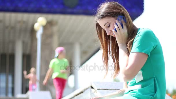 Joven wooman hermosa chica encantadora habla en su teléfono celular con amigos mientras está sentado en un parque — Vídeos de Stock