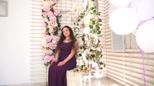 Jeune femme en robe violette s'assoit sur le banc de mariage avec des fleurs — Video