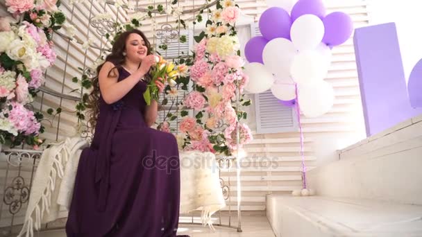 Mujer joven en vestido púrpura se sienta en el banco de la boda con flores — Vídeos de Stock