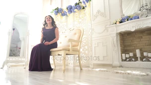 Jeune femme dans une robe de soirée violet assis sur le canapé dans le luxe Intérieur — Video