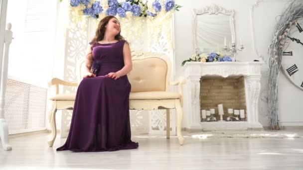 Jovem mulher em um vestido de noite roxo sentado no sofá em luxo Interior — Vídeo de Stock