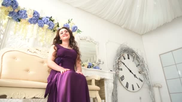 Jovem mulher em um vestido de noite roxo sentado no sofá em luxo Interior — Vídeo de Stock