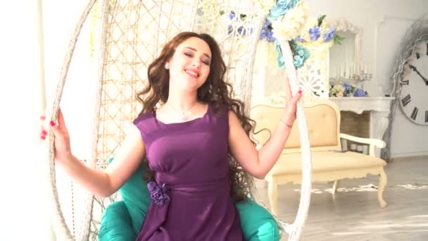 Belle jeune femme en robe de soirée est assis dans une chaise ronde en rotin sur l'intérieur de luxe — Video