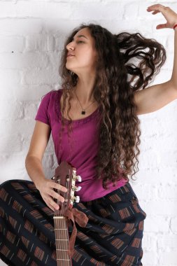Akustik gitar uzun etekle genç esmer kadın. Tuğla duvar arka plan